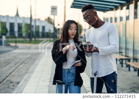 Handsome african american man and asian pretty girl go to business trip with suitcases and looking map at smartphone. 112271415