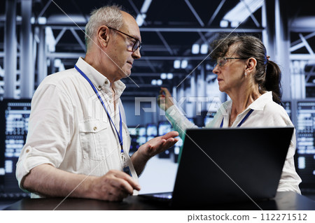 Senescent experts discussing how to best prevent strain on server hub systems caused by AI applications driving up power usage. Precise repairmen maintenancing rackmounts doing intense computations 112271512