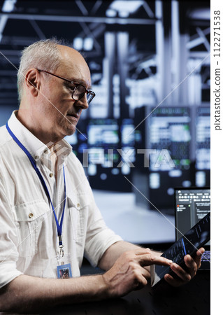 Senescent IT developer coding in high tech data center using javascript language. Qualified professional updating software on server rigs on laptop terminal, ensuring optimal performance and security 112271538