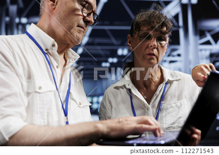 Senior teamworking colleagues running analysis on server cabinets helping businesses manage databases, host websites and store files. Proficient mechanics auditing high tech data center units 112271543