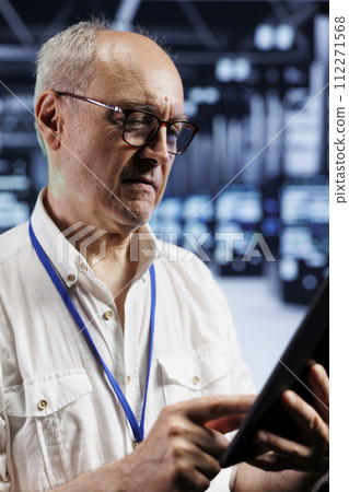 Qualified electrician in crypto mining farm with specialized electronics using Blockchain technology. Elderly wireman holding clipboard, inspecting asic server rows solving hashing operations 112271568