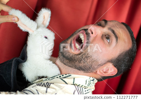 Close up Funny young adult man magician playing scary with rabbit out black hat 112271777