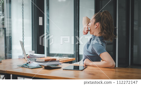 A woman experiences a moment of fatigue, yawning as she works on her laptop, signaling a need for a brief respite in her focused workday. A woman experiences a moment of fatigue, yawning as she works on her laptop, signaling a need for a brief respite in her focused workday. 112272147