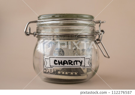 Saving Money In Glass Jar filled with Dollars banknotes. CHARITY transcription in front of jar. Managing personal finances extra income for future insecurity Saving Money In Glass Jar filled with Dollars banknotes. CHARITY transcription in front of jar. Managing personal finances extra income for future insecurity 112276587