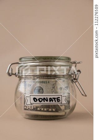 Saving Money In Glass Jar filled with Dollars banknotes. DONATE transcription in front of jar. Managing personal finances extra income for future insecurity Saving Money In Glass Jar filled with Dollars banknotes. DONATE transcription in front of jar. Managing personal finances extra income for future insecurity 112276589