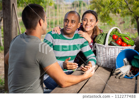 Cheerful couple of gardeners talking to neighbor outdoors Cheerful couple of gardeners talking to neighbor outdoors 112277488