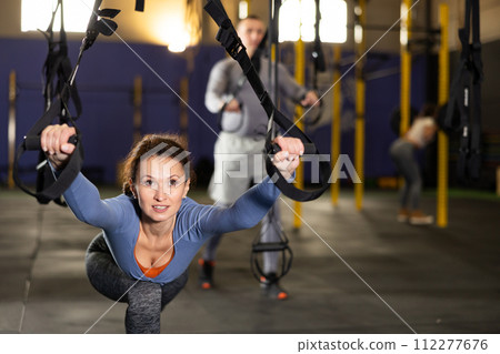 Female athlete with group working out on gymnastics rings at crossfit gym Female athlete with group working out on gymnastics rings at crossfit gym 112277676