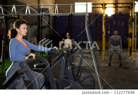 Concentrated woman working out on stationary air bicycle in gym 112277686