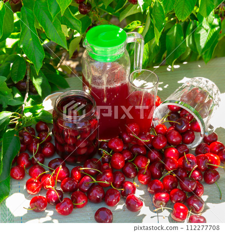 Fresh sweet cherries, mason jar of compote and juice in carafe in orchard Fresh sweet cherries, mason jar of compote and juice in carafe in orchard 112277708
