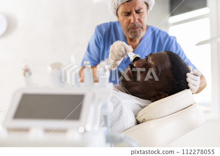 Male specialist uses ultrasonic import nozzle to care African man client face skin Male specialist uses ultrasonic import nozzle to care African man client face skin 112278055