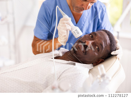 African man client undergoes facial skin care procedure using nozzle cold hammer whitening African man client undergoes facial skin care procedure using nozzle cold hammer whitening 112278127