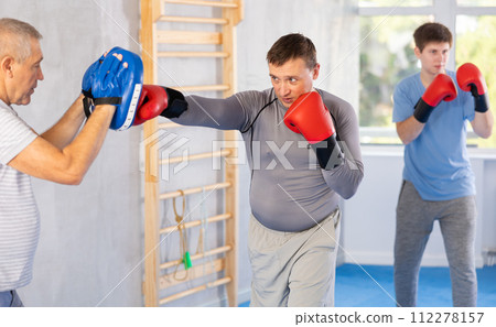 Man in boxing gloves practicing punches on mitts during self-defense course 112278157