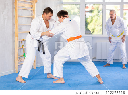 Jiu-jitsu master demonstrating basic grabs and throws in sparring with young fighter Jiu-jitsu master demonstrating basic grabs and throws in sparring with young fighter 112278218