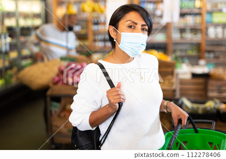 Woman in protective mask with bag and basket of vegetables at store 112278406