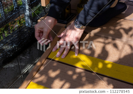 A man attaching anti-slip to a wooden deck sloop 112278545