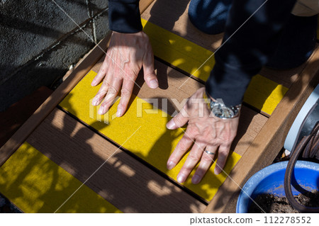 A man attaching anti-slip to a wooden deck sloop A man attaching anti-slip to a wooden deck sloop 112278552