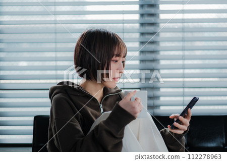 一位穿著家居服的女士坐在沙發上看著智慧型手機 一位穿著家居服的女士坐在沙發上看著智慧型手機 112278963