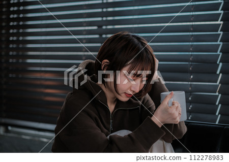 A woman in a loungewear sitting on a sofa and looking at a smartphone 112278983