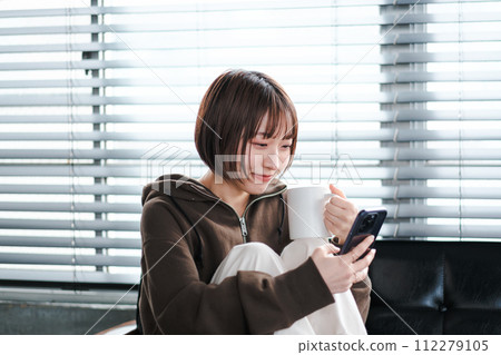 A woman relaxing in her loungewear while looking at her smartphone on the sofa in the morning 112279105