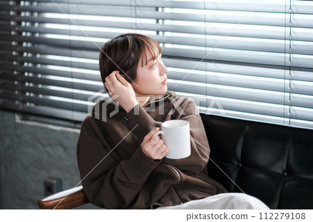 A woman relaxing in her loungewear while looking at her smartphone on the sofa in the morning A woman relaxing in her loungewear while looking at her smartphone on the sofa in the morning 112279108