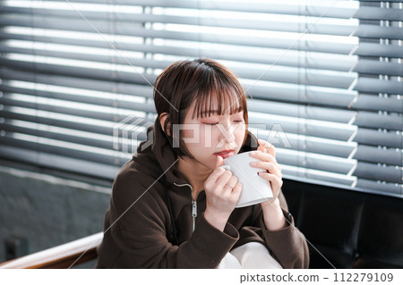 A woman relaxing in her loungewear while looking at her smartphone on the sofa in the morning A woman relaxing in her loungewear while looking at her smartphone on the sofa in the morning 112279109