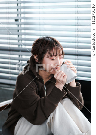 A woman relaxing in her loungewear while looking at her smartphone on the sofa in the morning A woman relaxing in her loungewear while looking at her smartphone on the sofa in the morning 112279110