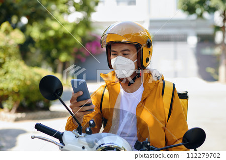 Serious delivery man sitting on motorbike when reading next order notification on smartphone 112279702