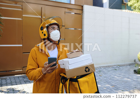 Delivery man in protective mask standing in front of house of customer Delivery man in protective mask standing in front of house of customer 112279737