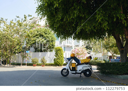 Delivery man relaxing on his scooter between orders Delivery man relaxing on his scooter between orders 112279753