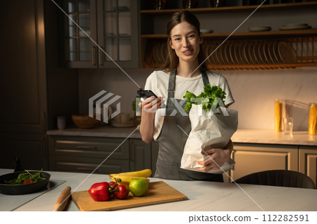 Woman Using Smartphone to Order Groceries in a Modern Kitchen  112282591