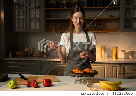 Smiling Video Blogger Presenting Homemade Croissants in a Modern Kitchen at Dusk 112282600