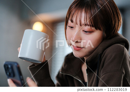 一位女士早上在房間裡喝咖啡時看著智慧型手機 一位女士早上在房間裡喝咖啡時看著智慧型手機 112283019