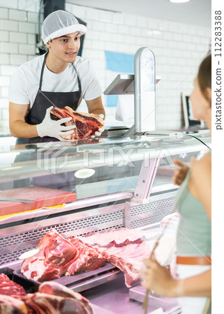 Young male seller offers girl to buy fresh beef entrecote boneless meat Young male seller offers girl to buy fresh beef entrecote boneless meat 112283388