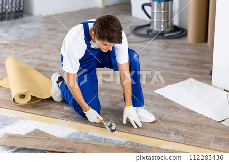 Young carpenter using rubber mallet to lay laminate flooring indoors 112283436