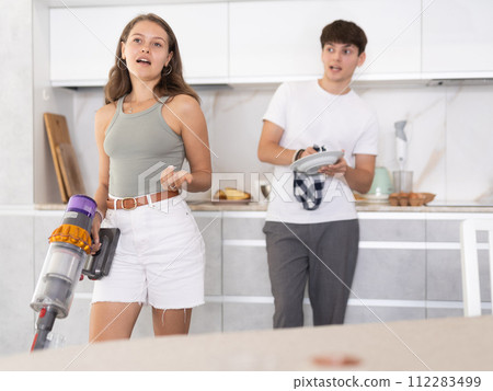Young woman vacuuming floor in kitchen at home 112283499