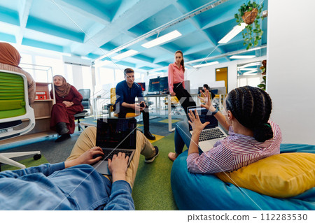 In a modern startup office, a diverse group of young and capable businesspeople engage in lively discussions about various projects, showcasing teamwork, innovation, and entrepreneurial spirit 112283530