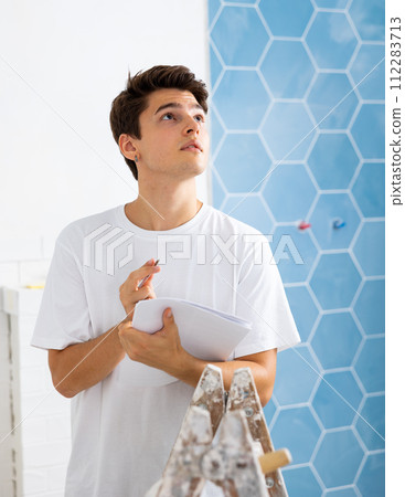 Young designer taking notes on papers while planning interior decoration 112283713