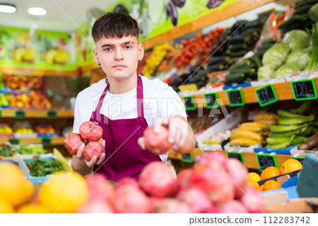 Hardworking young salesman puts pomegranates on the counter 112283742