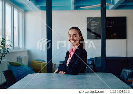 Successful young female leader in a suit with a pink shirt sitting in a modern glass office with a determined smile. Successful young female leader in a suit with a pink shirt sitting in a modern glass office with a determined smile. 112284333