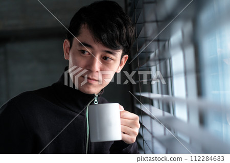 一個男人手裡拿著咖啡杯看著窗外 112284683