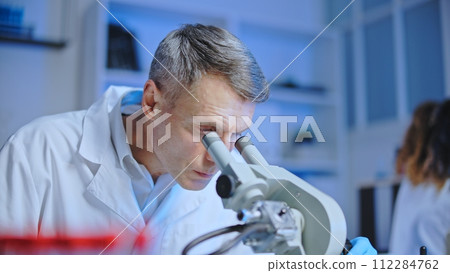 Focused medical technologist looking in microscope, examining blood samples 112284762