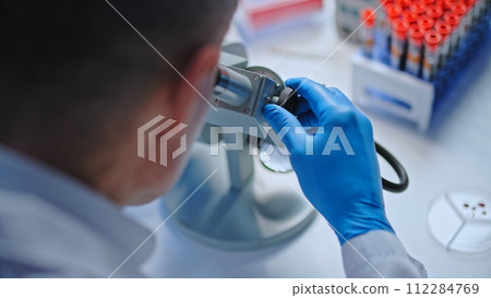 Hospital lab worker studying blood sample under microscope, disease diagnostics 112284769