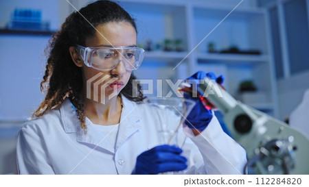 Busy female scientist in protective goggles mixing liquids, conducting laboratory experiment 112284820