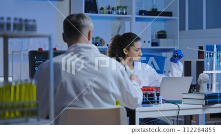 Serious laboratory assistant examining chemical flask with liquid, diagnostics 112284855