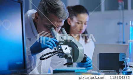 Focused lab scientists working on DNA research, examining samples under microscope 112284885