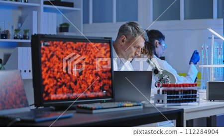 Phlebotomist examining blood samples under microscope in medical laboratory Phlebotomist examining blood samples under microscope in medical laboratory 112284904