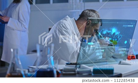 Lab worker looking at sample in microscope, unknown matter analysis on holographic screen 112285438