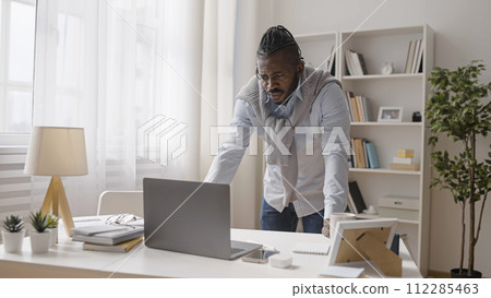 Concentrated man is looking at his laptop display, working on a difficult project 112285463