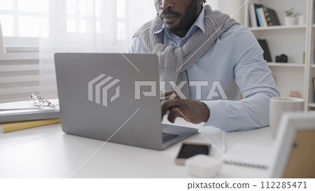 An African American man is working on his laptop, typing an article while sitting in his cozy home office An African American man is working on his laptop, typing an article while sitting in his cozy home office 112285471