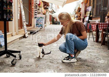 A young blonde woman leisurely strokes a black and white cat at a street market. A young blonde woman leisurely strokes a black and white cat at a street market. 112286440
